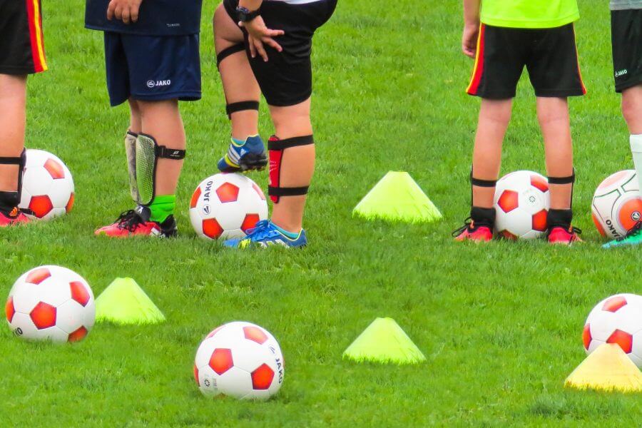 Viele Fußbälle auf dem Rasen, dazu Hütchen und einige Beine