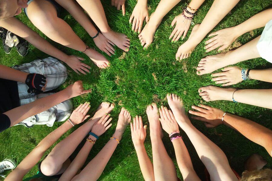 Eine Gruppe von Kindern sitzen auf einer Wiese. Sie formen einen Kreis mit ihren Händen und Füßen