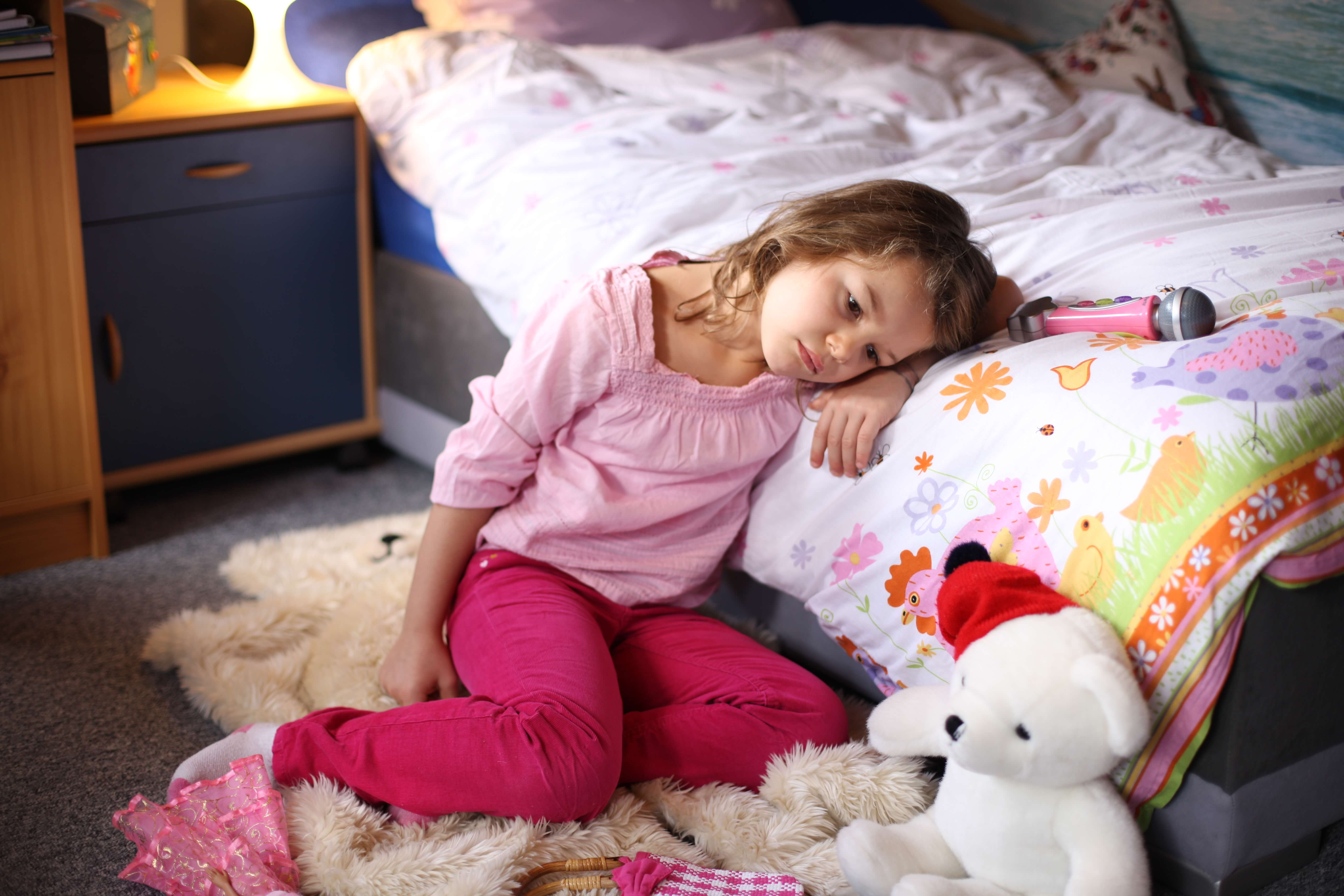 Trauriges Mädchen sitzt auf dem Boden und legt den Kopf auf ein Bett. Daneben Kuscheltiere und ein Mikrofon