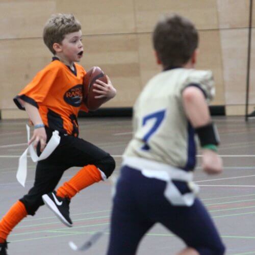 Zwei Jungen beim Football spielen in einer Turnhalle.