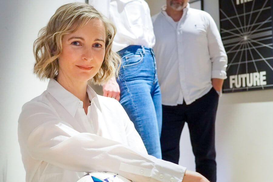 Drei Personen in einem Büro. Eine hält einen Fußball unter dem Arm