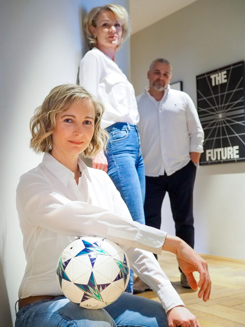 Drei Personen in einem Büro. Eine hält einen Fußball unter dem Arm