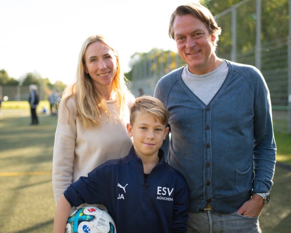 Zwei Erwachsene und ein Kind auf dem Fußballplatz. Der Junge hat einen Ball unter dem Arm