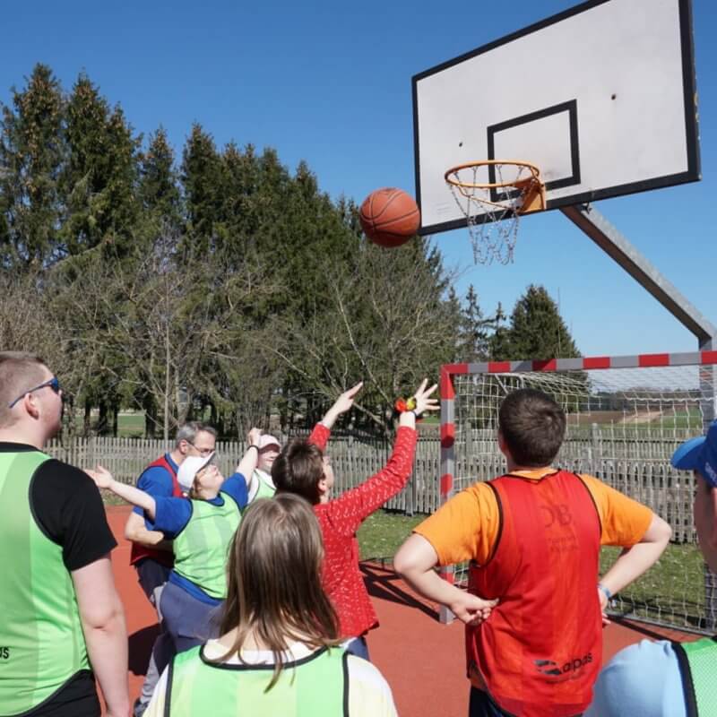 Einige Personen stehen vor einem Korb. Eine wirft einen Basketball