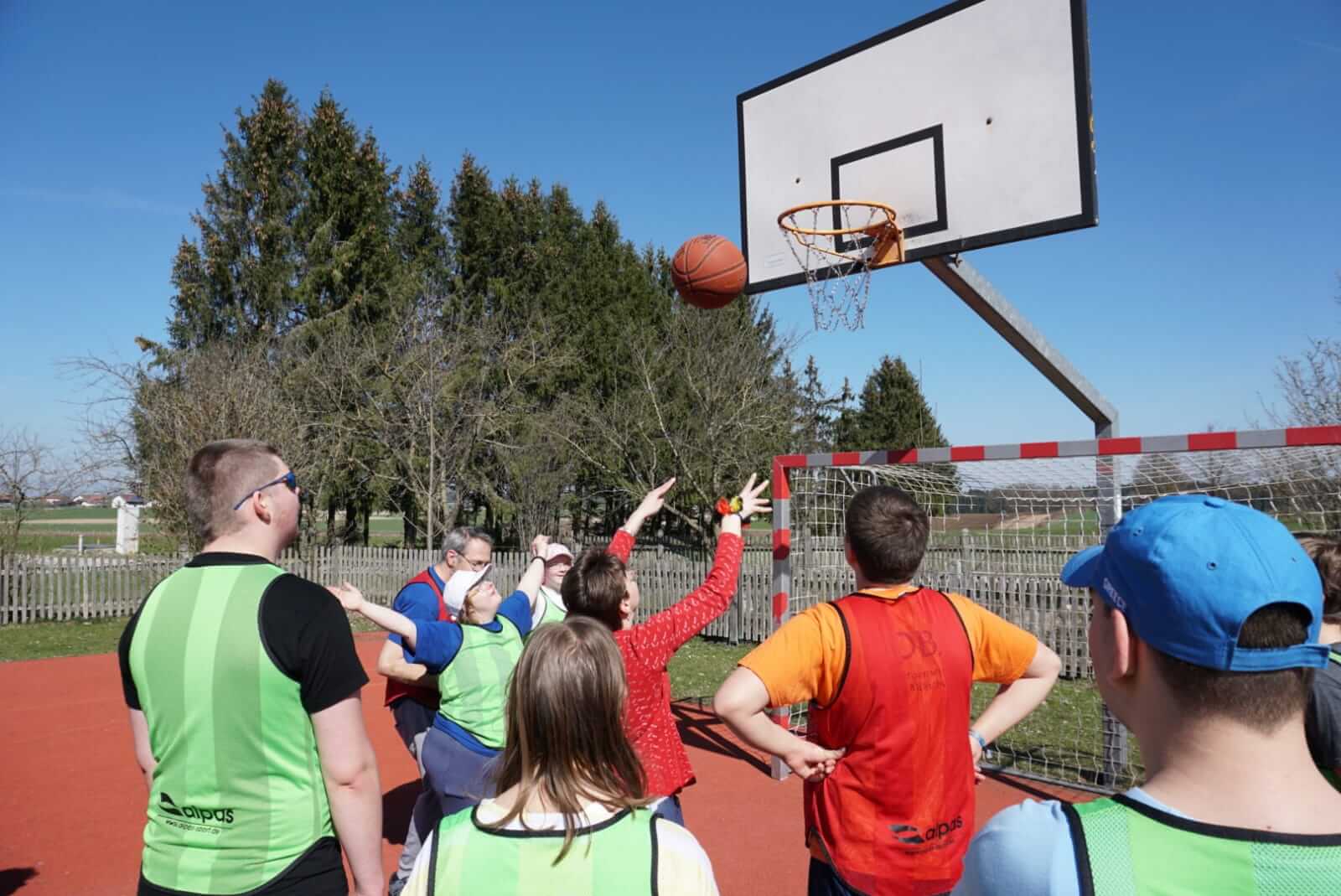 Einige Personen stehen vor einem Korb. Eine wirft einen Basketball