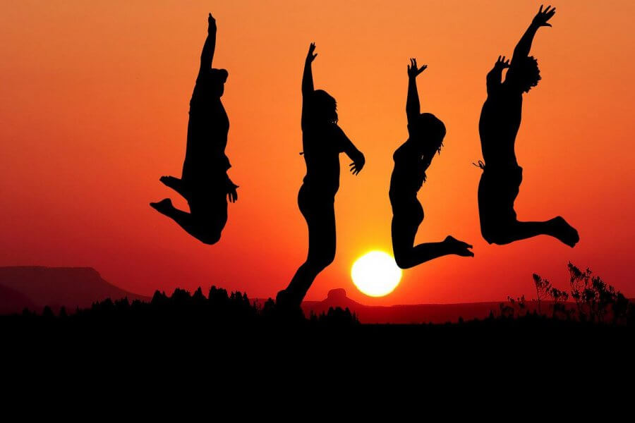 Vier Personen springen vor dem Sonnenuntergang. Sie stecken die Arme in die Luft