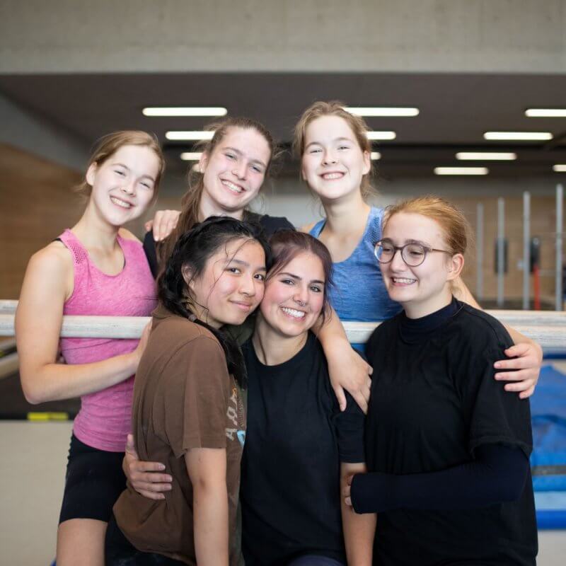 Sechs Mädchen stehen in einer Turnhalle und umarmen sich
