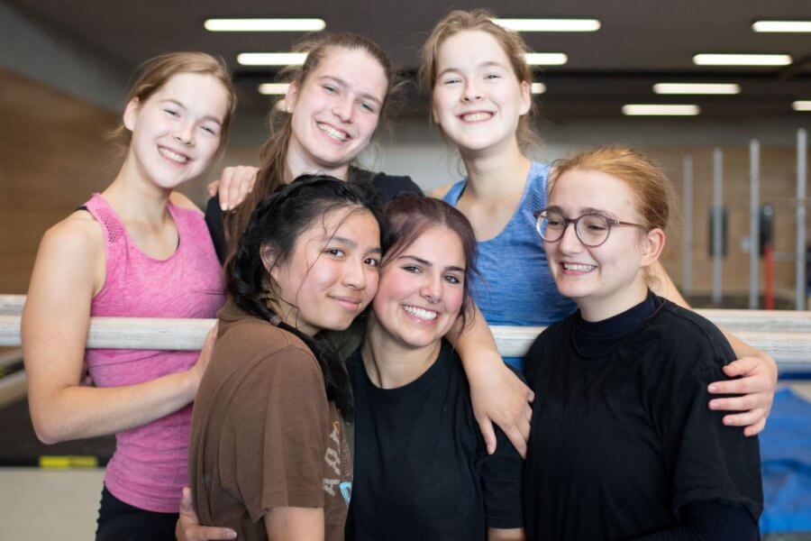 Sechs Mädchen stehen in einer Turnhalle und umarmen sich