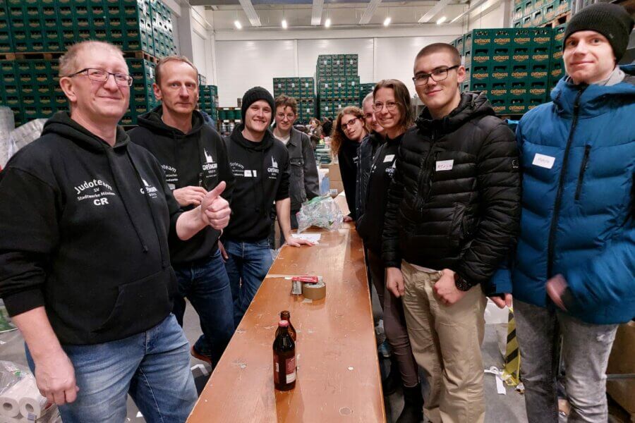 Gruppe von Erwachsenen stehen an einem Tisch. Im Hintergrund viele Paletten mit Getränkekisten