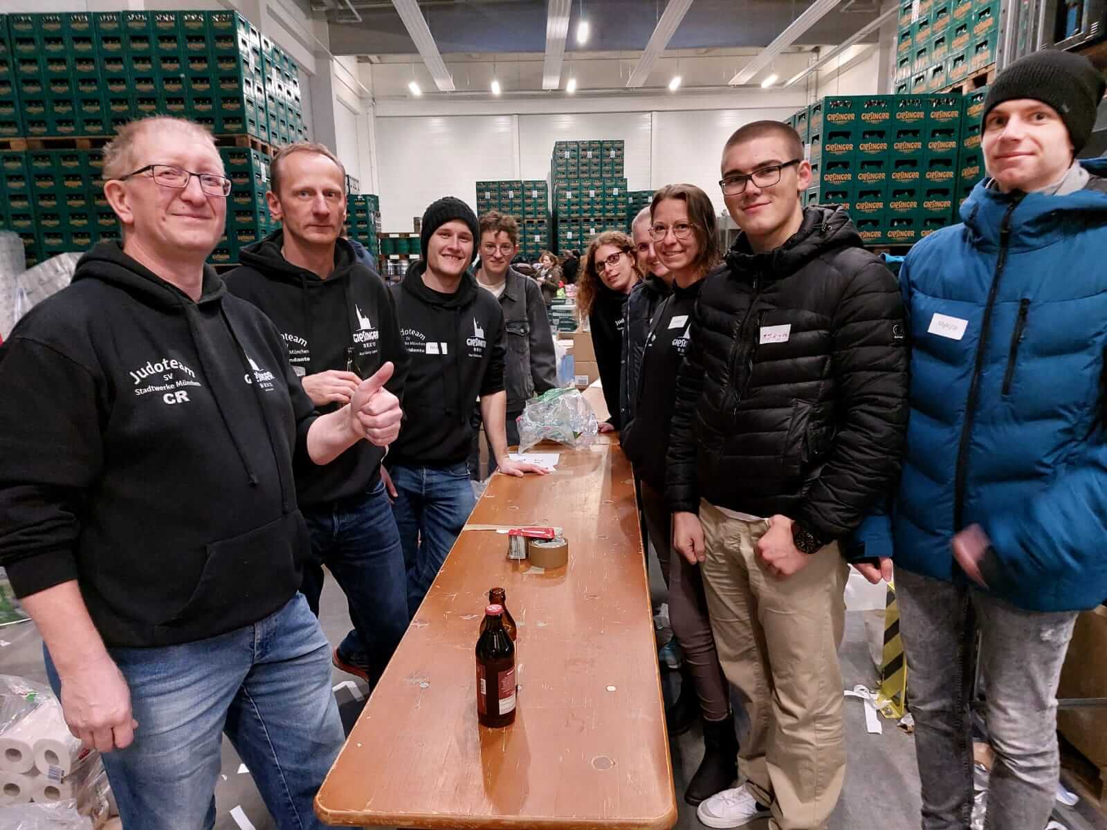 Gruppe von Erwachsenen stehen an einem Tisch. Im Hintergrund viele Paletten mit Getränkekisten