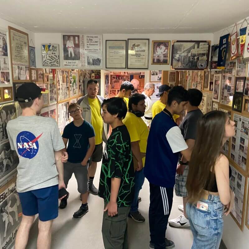 Gruppe von Jugendlichen in engen Raum. An allen Wänden hängen viele Bilder und Urkunden