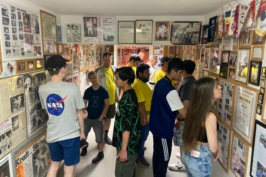 Gruppe von Jugendlichen in engen Raum. An allen Wänden hängen viele Bilder und Urkunden