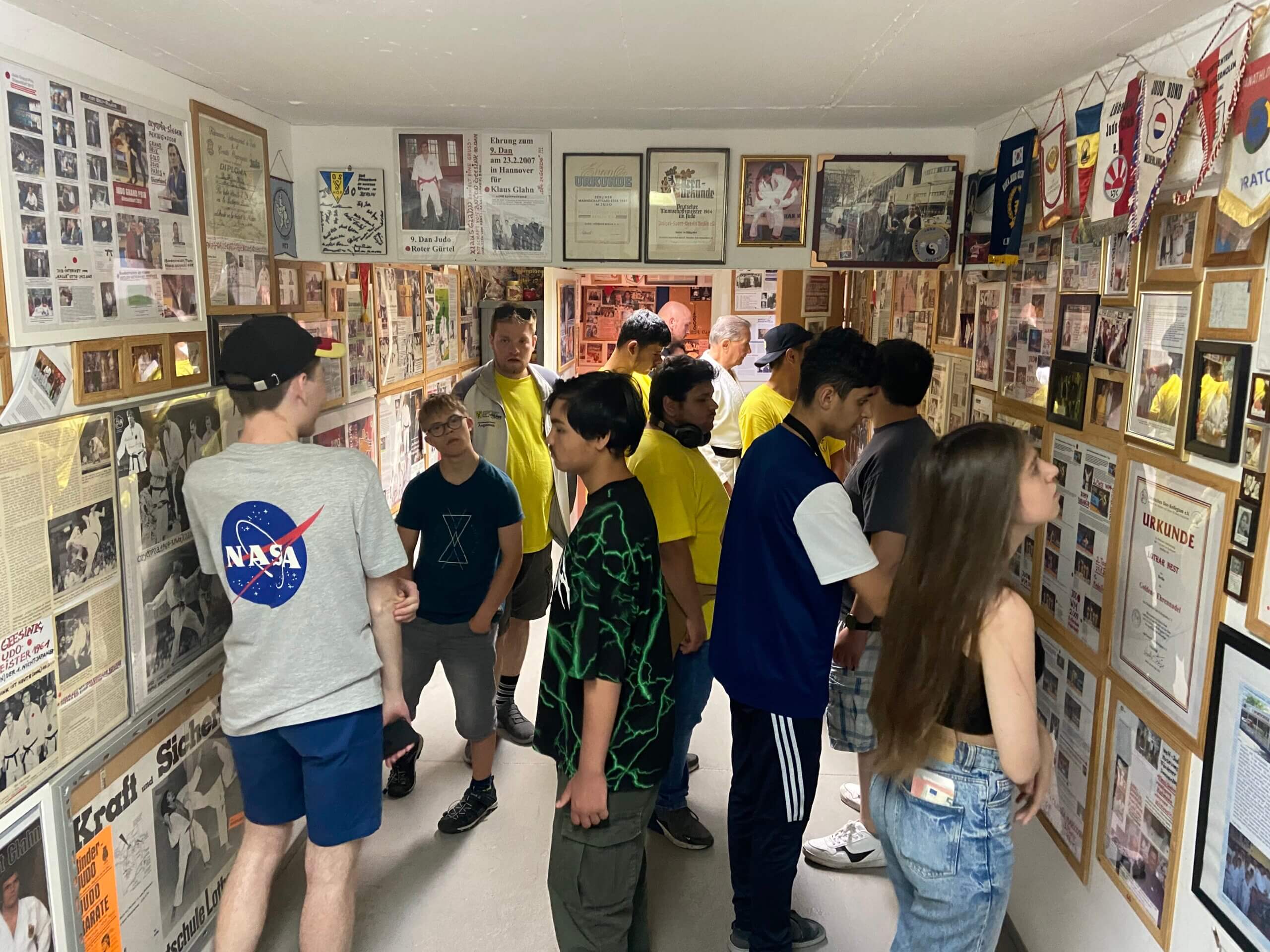 Gruppe von Jugendlichen in engen Raum. An allen Wänden hängen viele Bilder und Urkunden