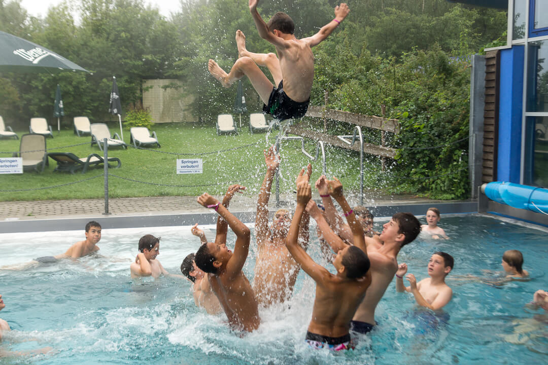 Gruppe von Kindern in einem Schwimmbecken. Ein Junge wird in die Luft geworfen