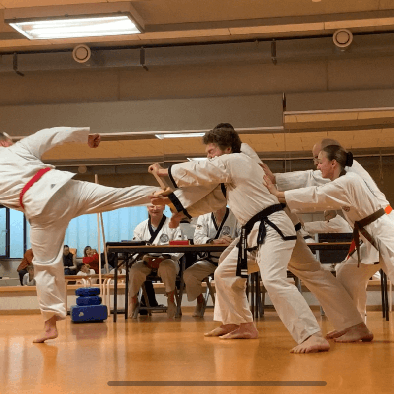 Mehrere Personen halten ein Brett. Ein Mann tritt gegen dieses