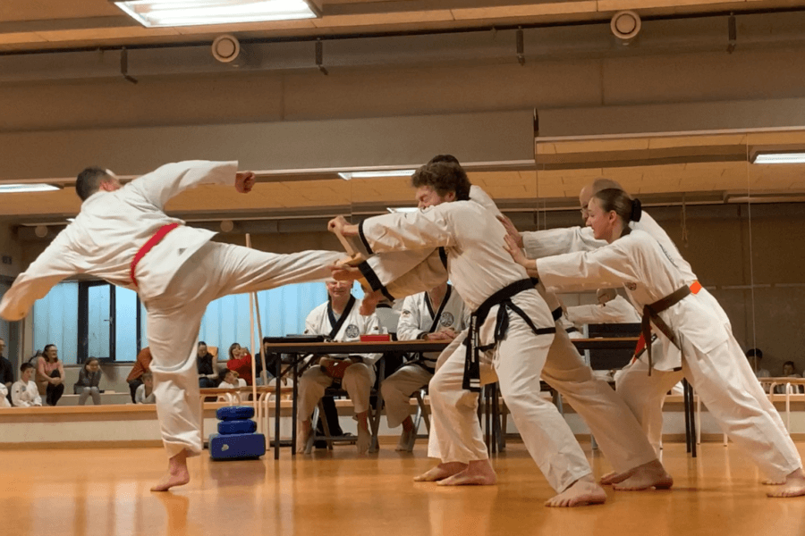 Mehrere Personen halten ein Brett. Ein Mann tritt gegen dieses