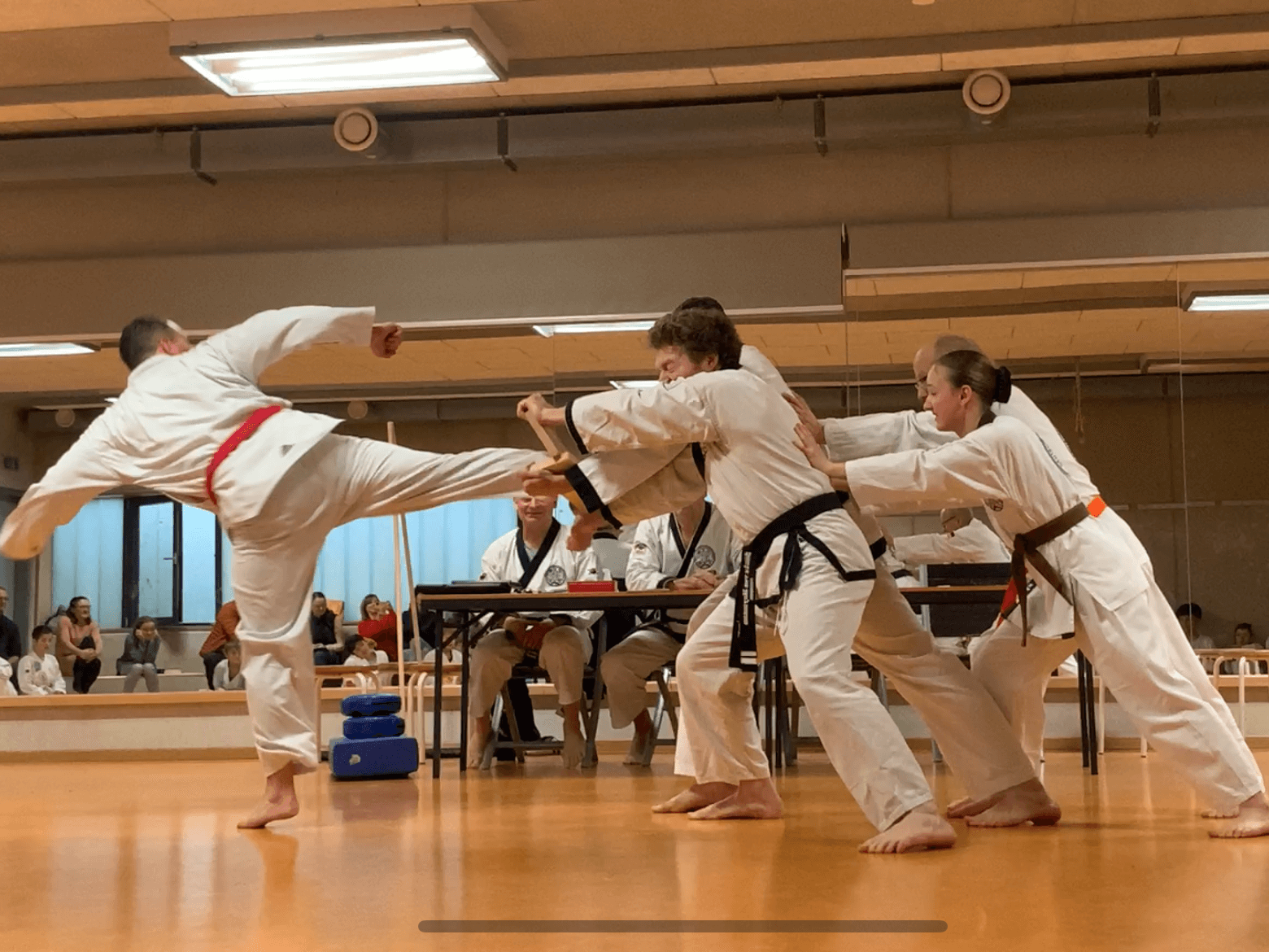 Mehrere Personen halten ein Brett. Ein Mann tritt gegen dieses