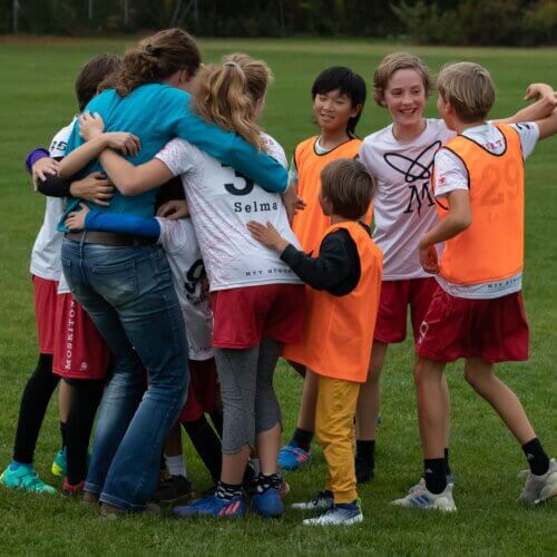 Eine Gruppe von Kindern umarmt sich auf einem Sportplatz