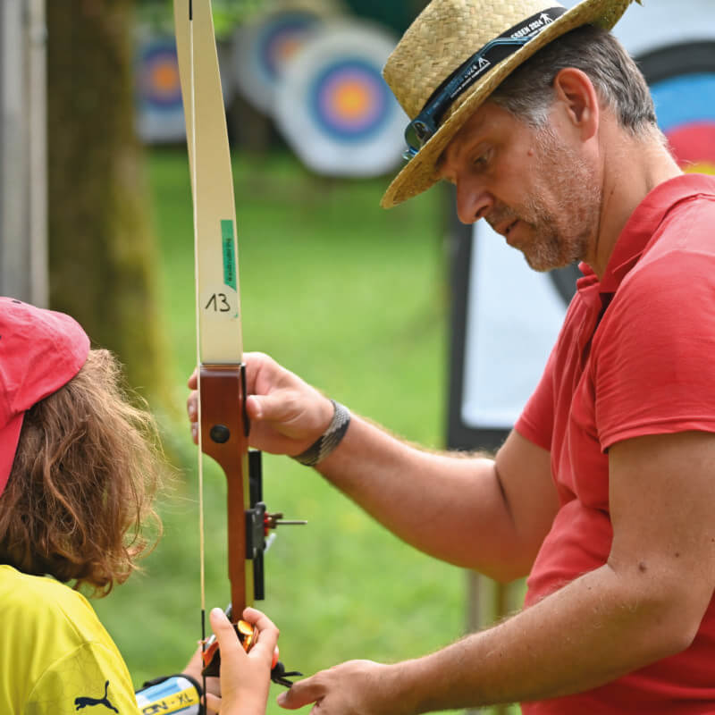 Ein Mann mit Strohhut hilft einem Kind beim Bogenschießen