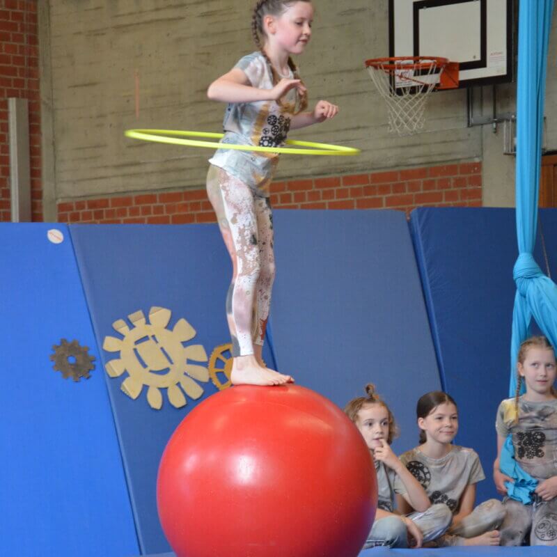 Kleines Mädchen mit einem Hula-Hoop-Reifen balanciert auf einem Gymnastikball