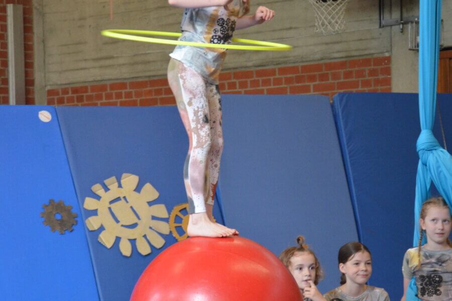 Kleines Mädchen mit einem Hula-Hoop-Reifen balanciert auf einem Gymnastikball