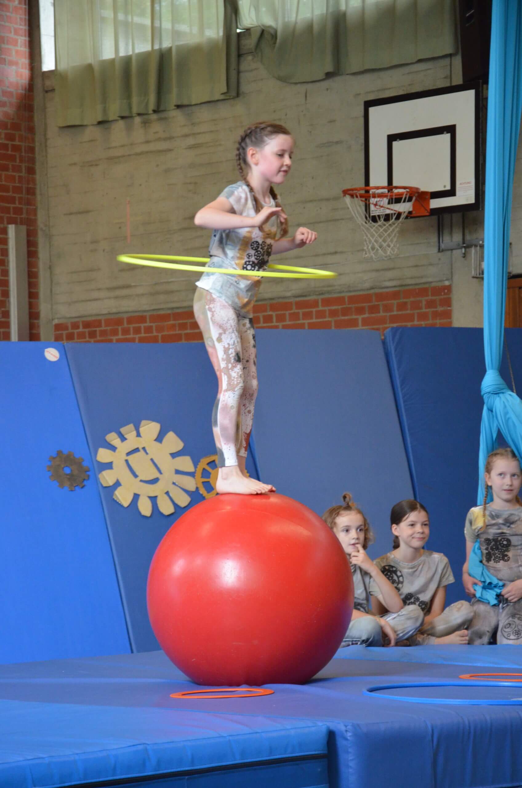 Kleines Mädchen mit einem Hula-Hoop-Reifen balanciert auf einem Gymnastikball